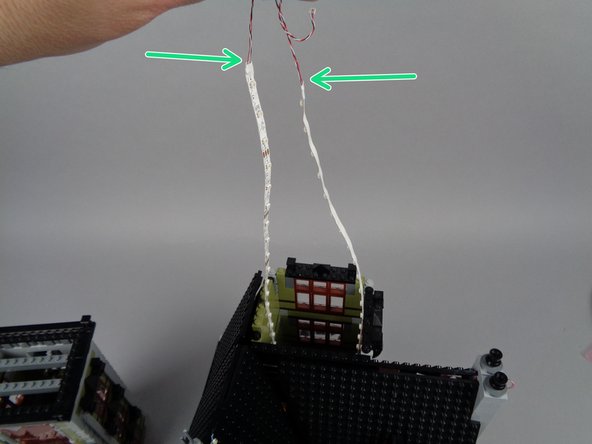 As shown by the green arrows in the first photo for this step, you should now have both light strips firmly attached to the lower section of the elevator shaft, with the two light strip wires extending out the top.