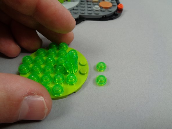 As shown in the photo for this step, remove two transparent bright green plates from the fountain base.  These should the the two plates at the end of the circle closest to the large jewel piece as shown in the photo.