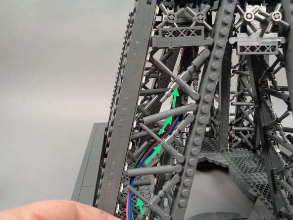 As shown by the green arrows in the first two photos for this step, feed the female plug of the inter-level connecting board into the center of pillar "A" of the tower middle section (this is the same pillar where you attached the first two light strips).