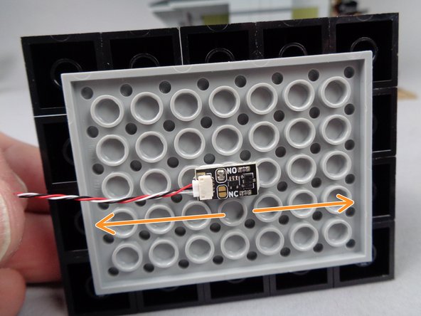 Attach the magnetic switch to the inside center of the pyramid roof section you removed in the previous step.  The two orange arrows show the direction in which the wire should extend: mount the switch so the long side of the switch is aligned with the long side of the roof.  The wire can extend toward either edge.