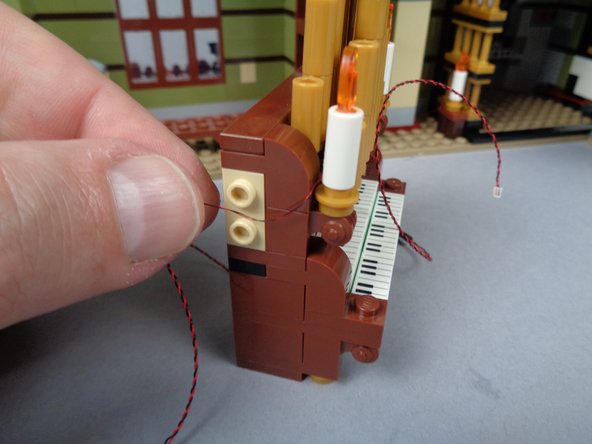 As shown in the first and second photos for this step, repeat this same process for the left candle, making sure to run the light wires between the studs under the brown side part and toward the back of the organ.