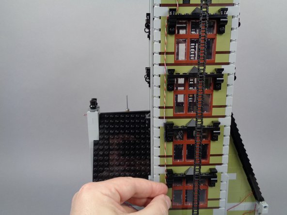 As shown in the photos for this step, continue feeding the magnet switch wire down the back of the tower wall by looping it through the parts of the window frames of lower windows.