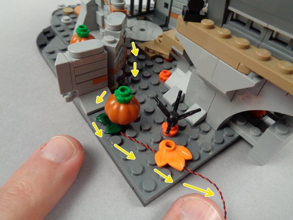 As shown by the yellow arrows in the third photo for this step, run the LED light wire backward and thread it below the plant leaf part under the pumpkin and at the back to hold the wire in place.