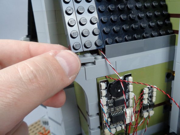 As shown by the orange circle in the third photo for this step, make sure the light bluish gray bricks are re-attached to the green wall bricks with the LED light wire running between the studs of the wall bricks.