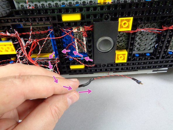 Route the speaker wire backward, through the holes in the black Technic frame, then around again as shown by the purple arrows in the first photo.