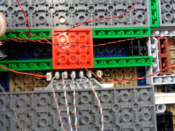 Attach two small sticky squares from the &quot;Lower Level Lights and Parts&quot; bag to the area under the castle by the 4x4 red plate as shown.