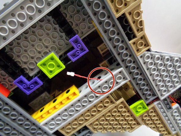 As shown in the third photo, carefully re-attach the light bluish gray plate, passing the red wire between it and the Technic brick above.  When re-attaching the plate, make sure that the red wire passes between the studs of the light bluish gray plate, not on top or over any studs.