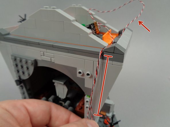 As shown by the green circle and arrow in the second photo for this step, remove the dark bluish gray slope piece from the back of the town hall roof, to make room to run the two wires.