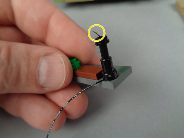 As shown in the first photo, carefully press the lamp post back down on the stud in its original location.  The red arrow in the photo shows how the LED wire should be positioned facing the back side of the base section.