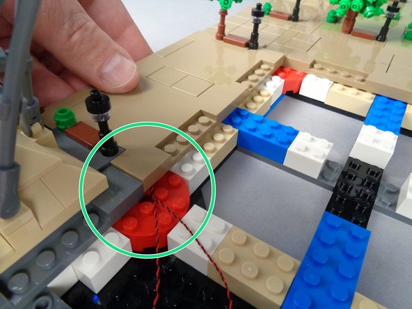 With the LED light wires for both lamp posts passing out of the bottom corner of the panel (as shown by the green circle in the first photo for this step), carefully but firmly press down on Panel 1L to re-attach it.