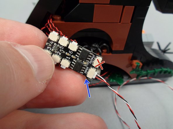 As shown by the green arrow in the second photo for this step, connect one end of the 3-wire connecting cable to the PIXEL1 plug on the main lighting effect controller.