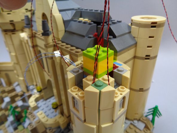 As shown in the first and second photos, carefully re-attach the tower side and top parts you removed earlier, always making sure the window light wires run upward and also that they are not pinched on top of any studs.