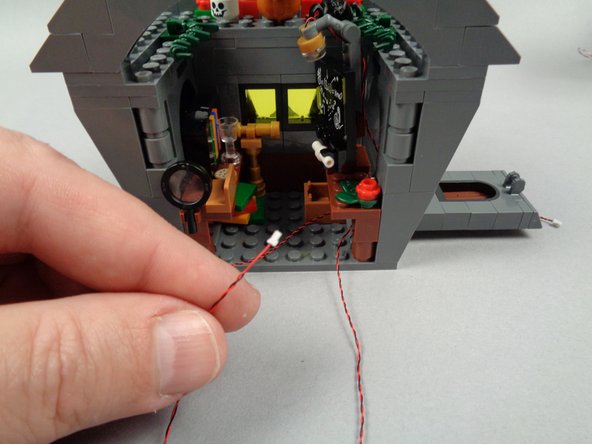 As shown in the first photo for this step, pass the light wire for the blackboard light back under the desk and out through the back of the house as shown in the second photo.