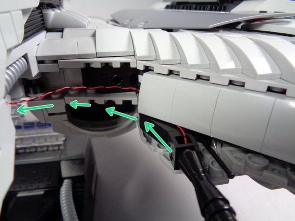 As shown by the green arrows in the first photo for this step, carefully pass the light wire behind the armor section just above the gun, to hide the wire.