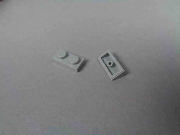 As shown in the first photo for this step, there are two light bluish gray LEGO pieces in a bag inside of BOX #1: a 1x2 plate and a 1x2 slope.