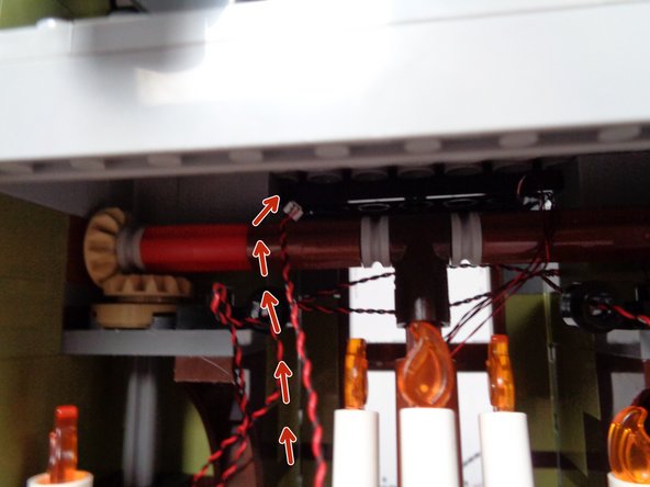 As shown by the red arrows in the second photo for this step, pass the plug for the light wire ABOVE and OVER the long axle that moves the front door.