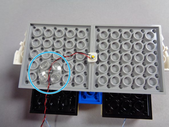 As shown in the first photo for this step, take the warm white Pico LED light with longer wire and attach one of the small sticky squares underneath.  The sticky squares will also be found inside your &quot;Roof Parts&quot; bag.