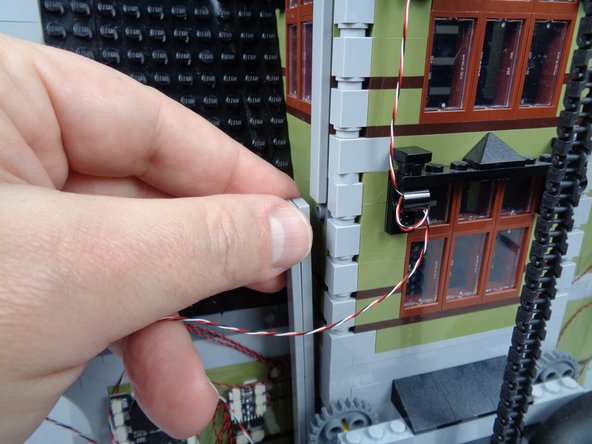 As shown in the photos for this step, finish routing the magnetic switch wire by running it behind one of the long LEGO tiles used to support the tower.