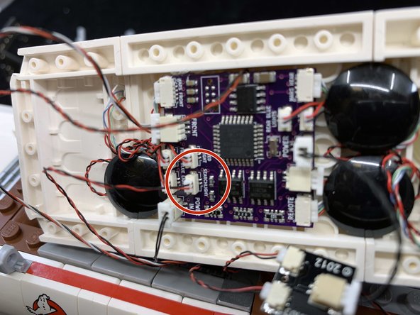 As shown in the second photo, re-attach the parts you removed in Step 15.  The searchlight wire should extend out from under the light bluish gray slope parts as shown in the second photo.