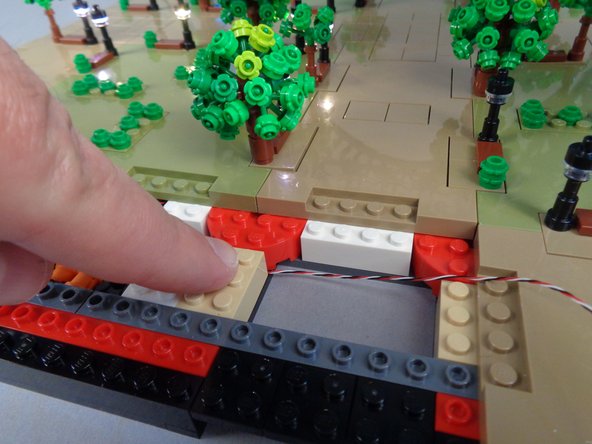 As shown in the photos for this step, temporarily lift the 2x3 tan brick and run the control cable between the studs on the black bottom plate, then re-attach the tan 2x3 brick on top of the control cable.