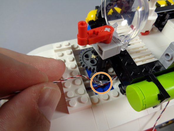 As shown by the orange circle in the second photo for this step, you will now pass the control wire and its plug down through the hole in the blue plate on the roof.