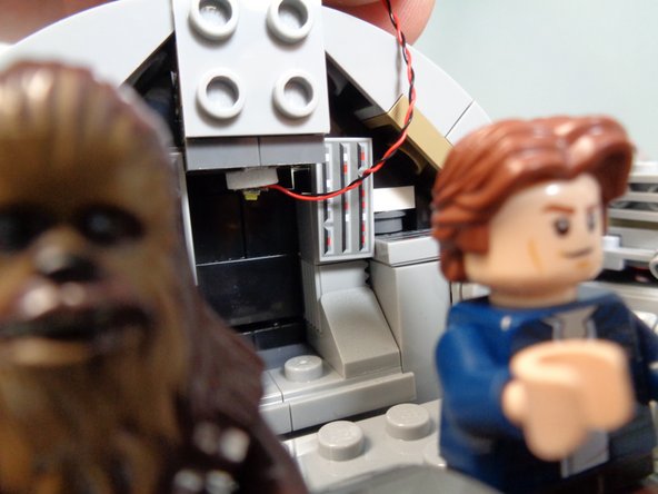 Take a Pico LED light and small sticky square, and mount the light to the center back of the cockpit door as shown in the first photo.