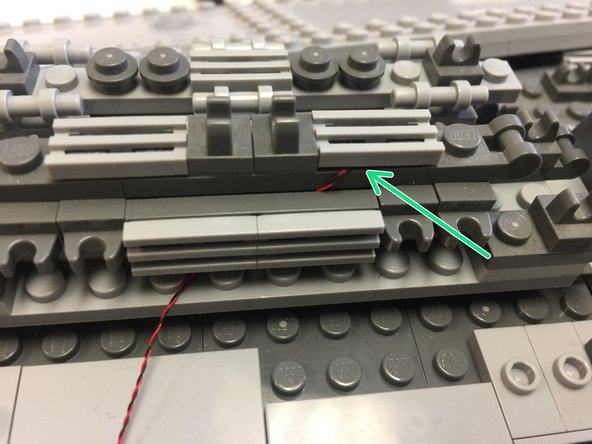 As shown in the illustration in the first step, you also need to mount two blue lights in the front center section of the ship.  The second photo in this step shows how to run the wires and attach the blue light under a grille tile piece (see green arrow).