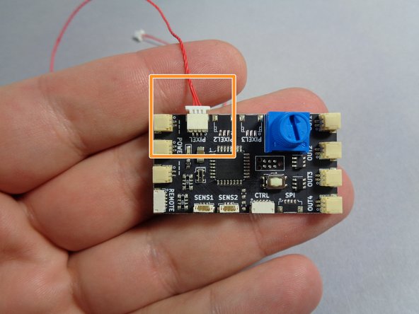 Take one of the red connecting cables and plug one end of the cable into the PIXEL (or PIXEL1) plug on the TRUNK08 master controller board, as shown by the orange square in the photo.