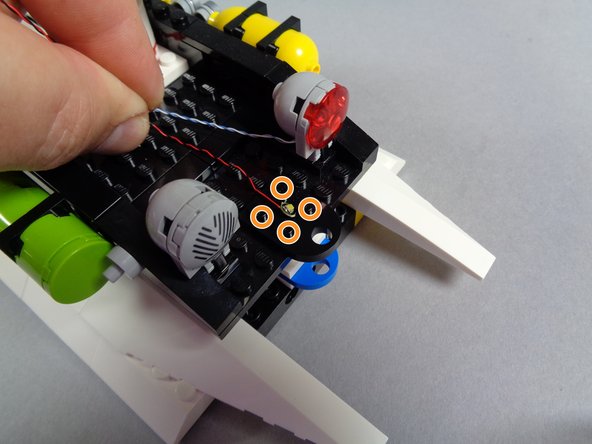 The four orange circles in the first photo for this step show the four studs on top of the black roof plate between the red roof light and the silver siren.