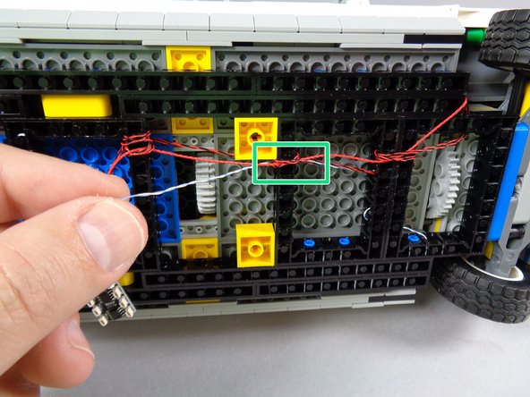 As shown by the green rectangles in the first and second photos for this step, continue passing the hood spot light wire back through holes in the black Technic frames until it reaches the area of the BRANCH09X adapter.