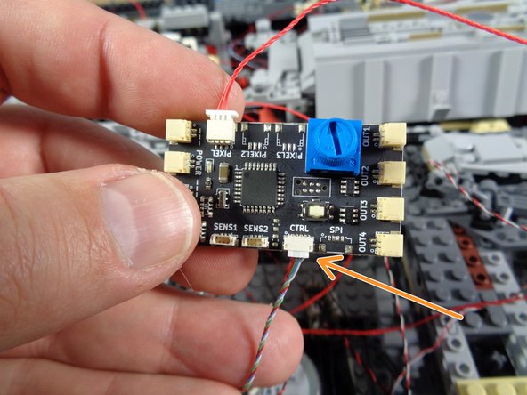 As shown by the orange arrow in the first photo, connect the small 4-wire plug from the laser sound module to the connector on the TRUNK08 master controller labeled &quot;CTRL.&quot;