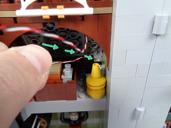 As shown by the green arrows in the third photo for this step, feed the end of the long wire into the center section attic space and back through the gap in the roof.