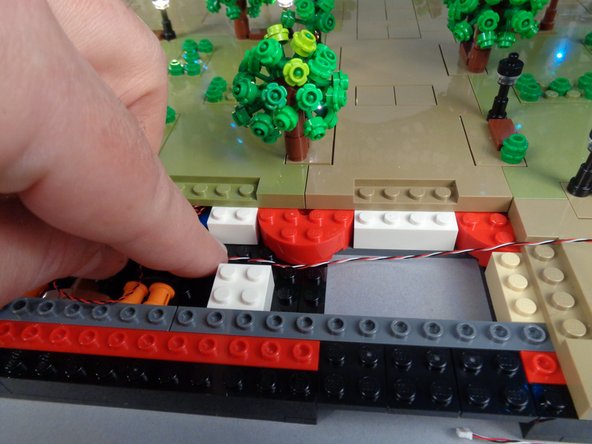 As shown in the photos for this step, temporarily lift the 2x3 tan brick and run the control cable between the studs on the black bottom plate, then re-attach the tan 2x3 brick on top of the control cable.