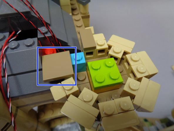 As shown by the blue rectangle in the third photo, attach the 2x2 dark tan tile on top of the light blue brick and one stud of the roof.