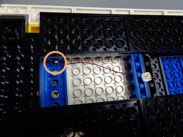 As shown by the orange circle in the third photo for this step, pass the LED light wire through the top hole in the blue Technic plate at the back of the roof.