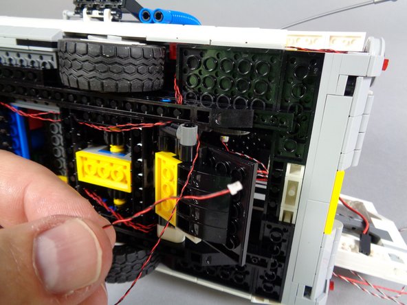 As shown by the blue arrow in the first photo, pull the tail light wire tight, and pass it through the same hole in the black Technic frame as the other two tail light wires pass through.