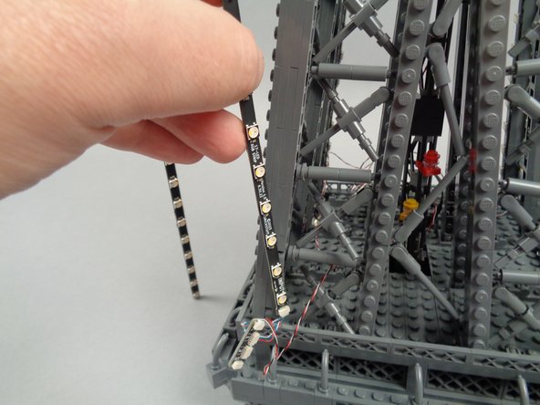Remove the backs of the sticky dots on the second light strip (connected to plug #2 of the adapter board), and attach the strip to the tower frame as shown in the photos for this step.