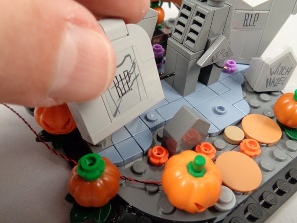 As shown in the first and second photos for this step, remove the large &quot;RIP&quot; gravestone to make room to run the LED light wire. Re-attach the gravestone on top of the wire.