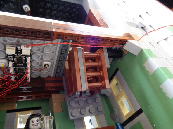 It may be difficult to separate the bricks enough to run the red wire.  Move slowly and keep separating until there is enough room to pass the red wire BETWEEN the studs on top of the floor support. as shown by the blue arrow in the first photo.