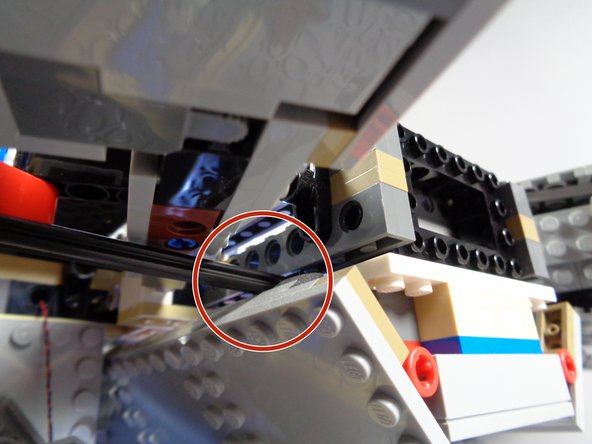 As shown by the red circle in the second photo, carefully pass the black axle through the outer Falcon frame into the boarding ramp area.