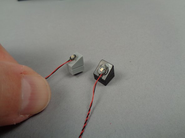 As shown in the photo for this step, remove the backs of the sticky discs and attach the LED lights to the two slopes with their wires facing downward.