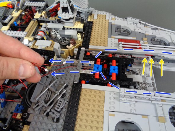 As shown by the blue dotted lines and arrows in the second photo, carefully route the mabdible light wires down the inner sides of the Falcon and back toward the second BRANCH09X adapter board.