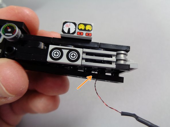 Once the plate has been loosened, as shown by the orange arrow in the second photo, carefully pass the wire for the speedometer light from the back side of the dashboard through to the front.