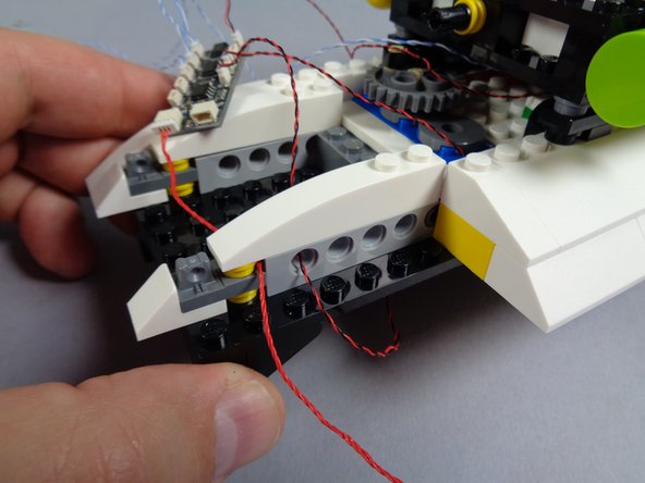 As shown in the first photo for this step, re-attach the white slope on top of the Technic brick and yellow plate that holds the red wire in place.