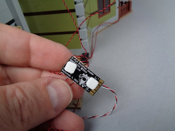 As shown in the photos for this step, use two sticky squares to attach the second BRANCH06X adapter board to the back wall of the mansion.