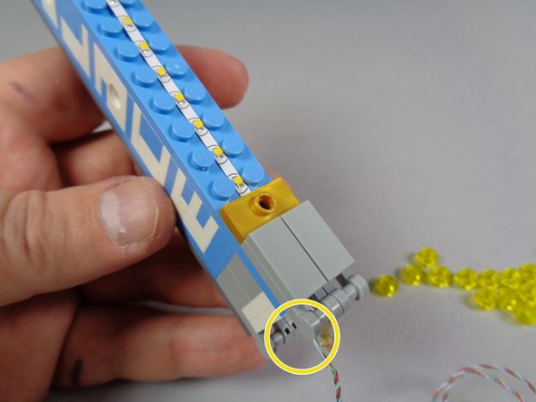 As shown by the blue arrows in the second photo, use another gold jumper with hole to secure the bottom end of the light strip, and carefully re-attach one of the two bottom gray plates with tile on top.