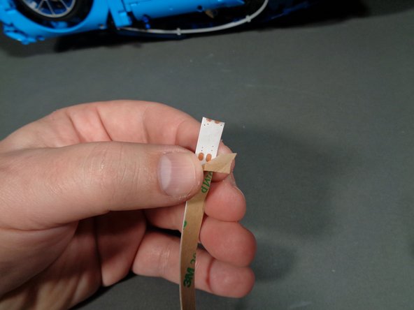 As shown in the first photo for this step, carefully peel the self-adhesive backing from the first light strip and attach it along one side of your Bugatti frame.