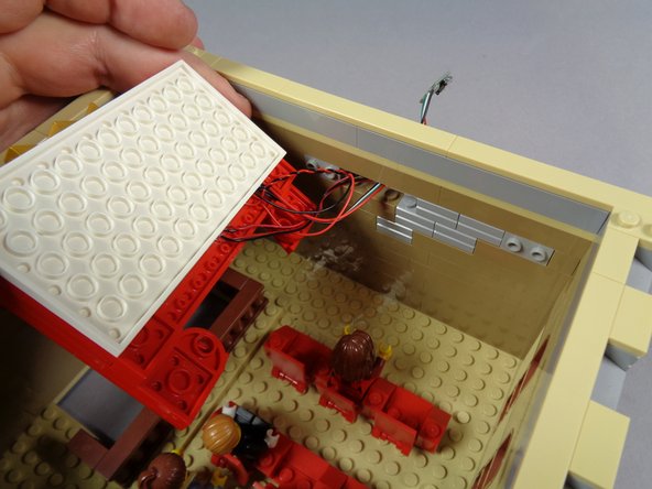 As shown by the two photos in this step, next you will pass the video player wires through the hole in the wall that you made earlier by removing the two light bluish gray bricks.