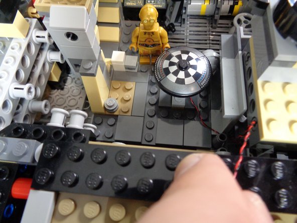 The red dotted line in the third photo shows where the wire should run, after the seats have been re-installed.  The light wire will run under the seats and through the stud hole in the black Technic brick as shown by the red circle.