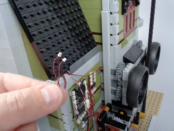 As shown in the first photo for this step, pull the two red LED light wires all the way through the gap between the roof and the back wall.